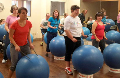 A group of people standing with exercise balls and playing them like a drum.